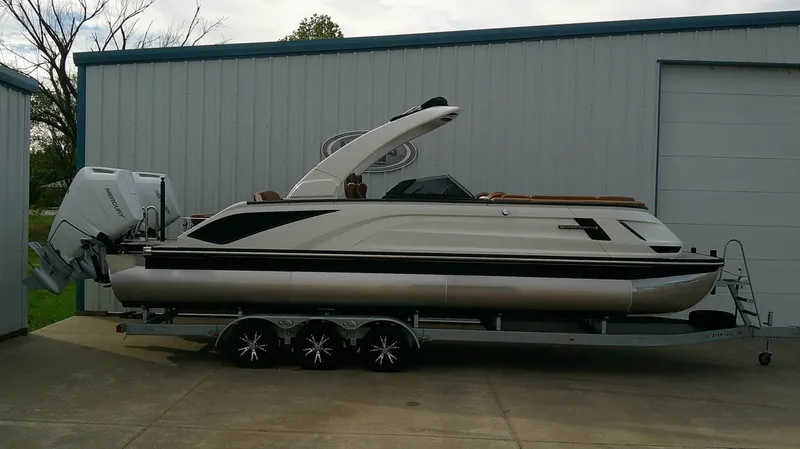 Slide: The Image of A sleek 2027 Bennington 27 QXSBA pontoon boat on a trailer in front of a building. - 3