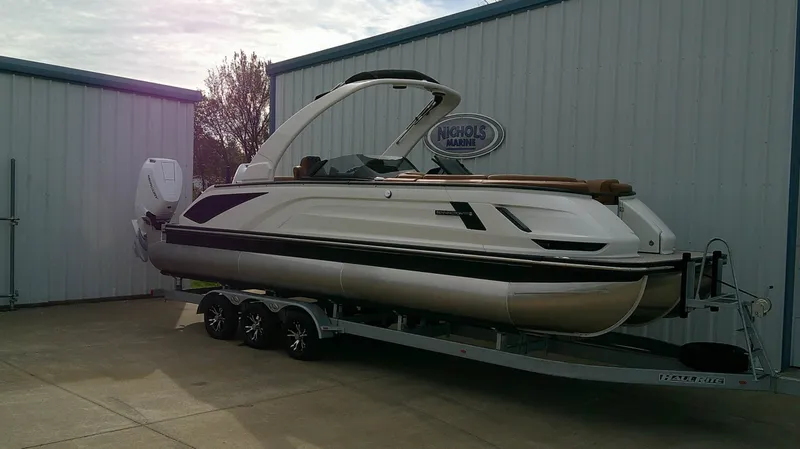 The Image of A sleek Bennington 27 QXSBA pontoon boat from 2027 sits on a trailer outside a building. - 0
