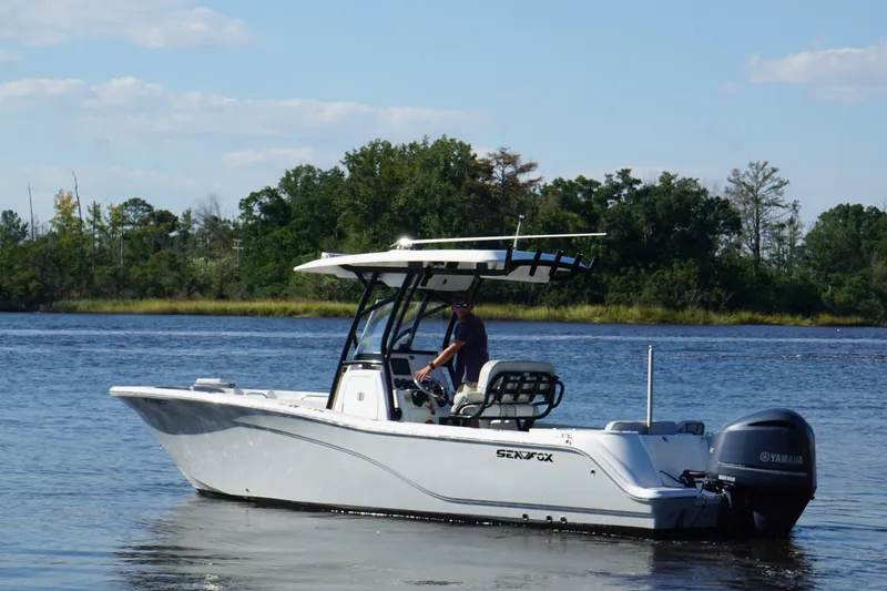 Slide: The Image of 2021 Sea Fox 248 Commander boat cruising on a calm lake with lush green shoreline. - 2