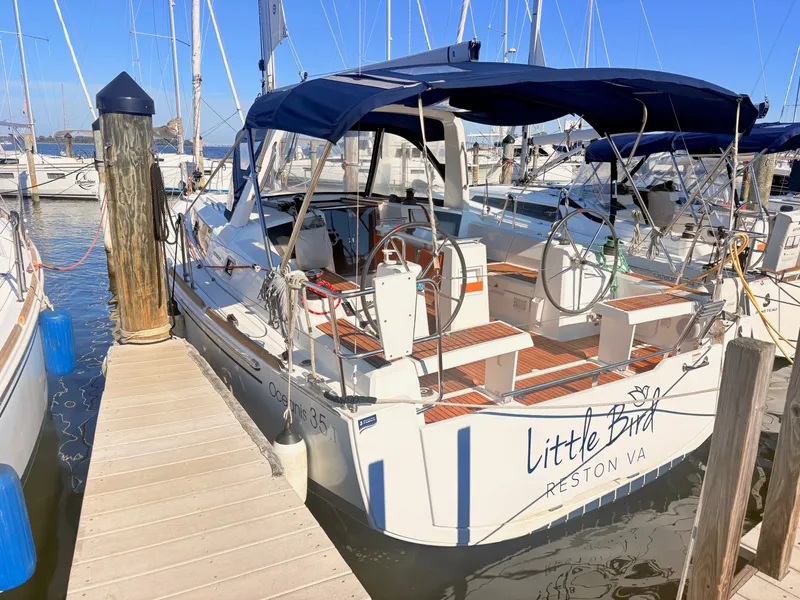 Slide: The Image of A 2020 Beneteau Oceanis 35.1 docked, featuring a blue canopy and wooden deck. - 0