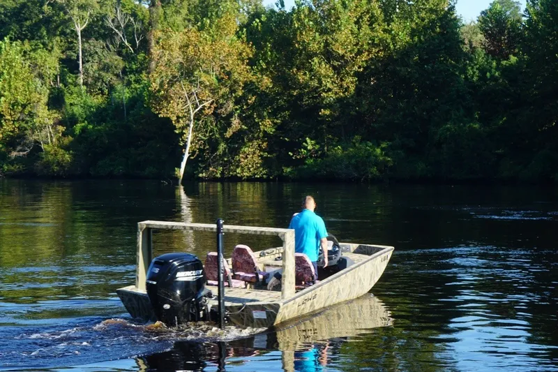 Slide: The Image of Man driving Lowe Outlet 20 boat on a serene river, surrounded by lush greenery. - 4