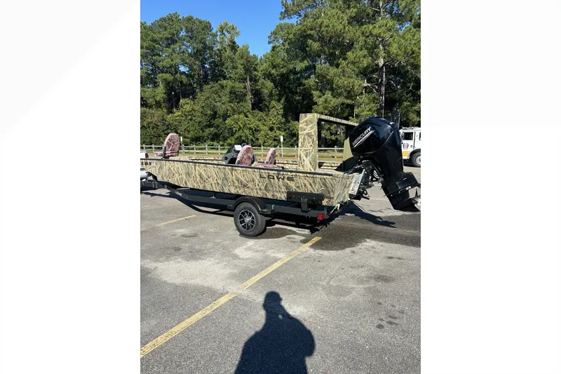 Slide: The Image of 2025 Lowe Outlet 20 boat with camouflage design, parked outdoors on a sunny day. - 8