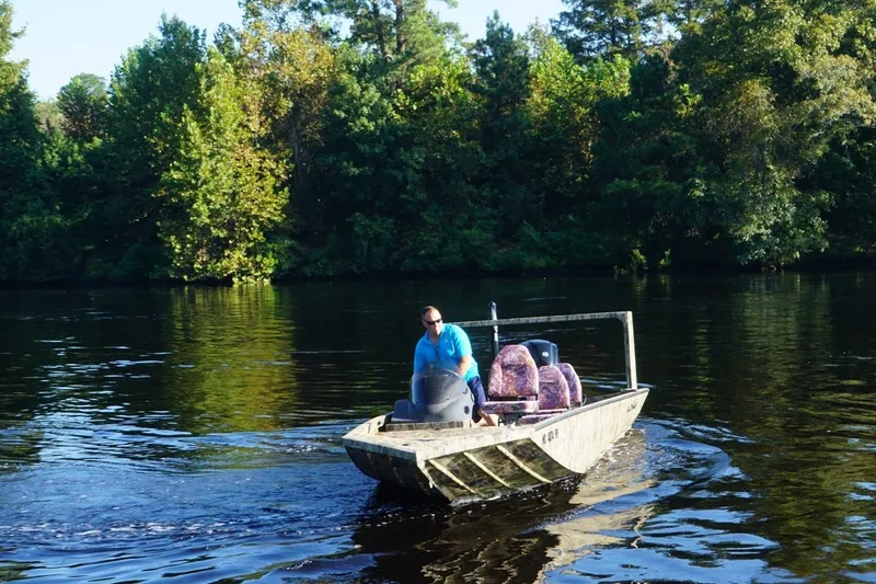 Slide: The Image of Man driving 2025 Lowe Outlet 20 boat on a serene lake surrounded by trees. - 3