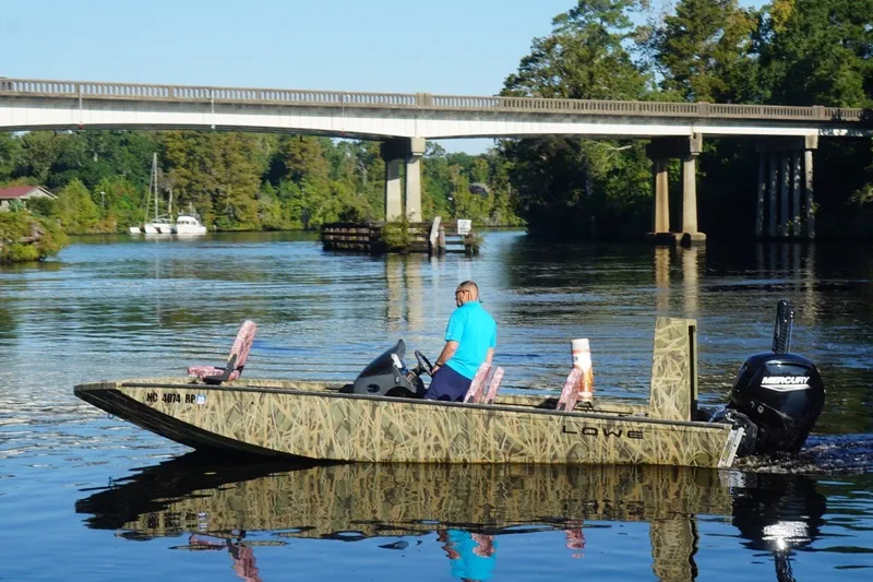 Slide: The Image of A Lowe Outlet 20 boat from 2025 cruising on a scenic river under a bridge. - 7
