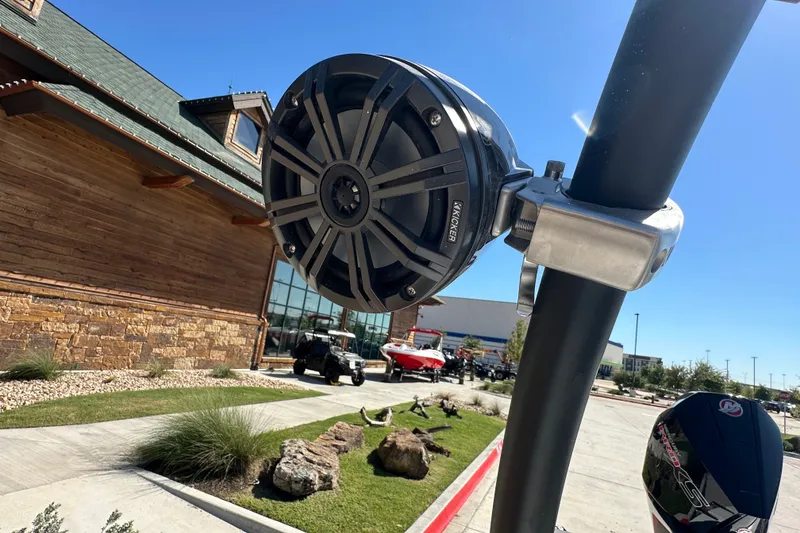 Slide: The Image of Outdoor speaker on Tahoe T21 boat, 2027 model, near rustic building and parked vehicles. - 16