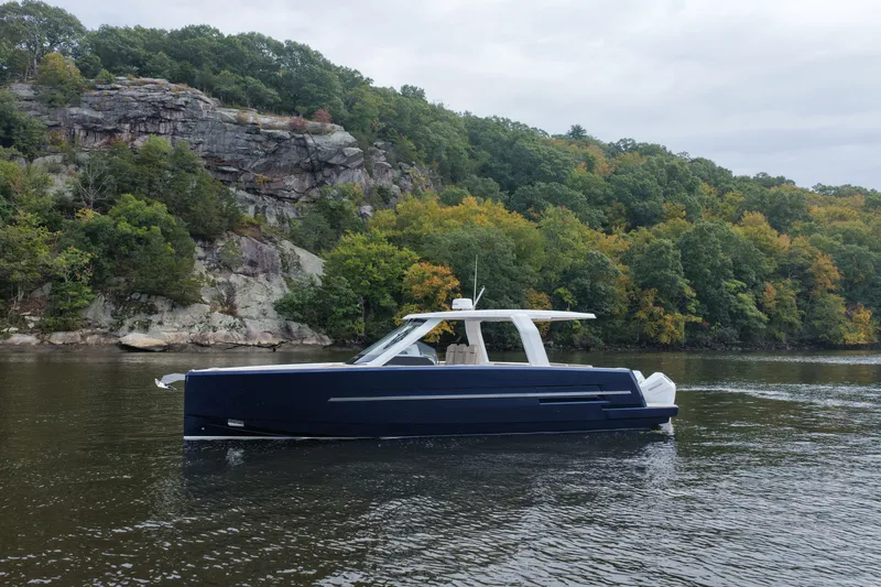 The Image of The 2027 Fjord 39 XP cruises on a calm river, surrounded by wooded cliffs. - 1