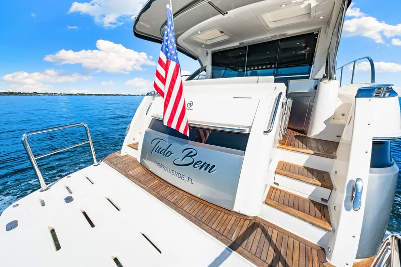 Slide: The Image of 2024 Riviera 4600 Sport Yacht Platinum Edition on water, rear view with American flag. - 21