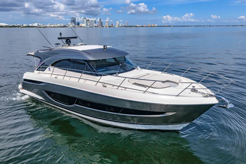 The Image of 2024 Riviera 4600 Sport Yacht Platinum Edition cruising on calm waters with city skyline backdrop. - 0