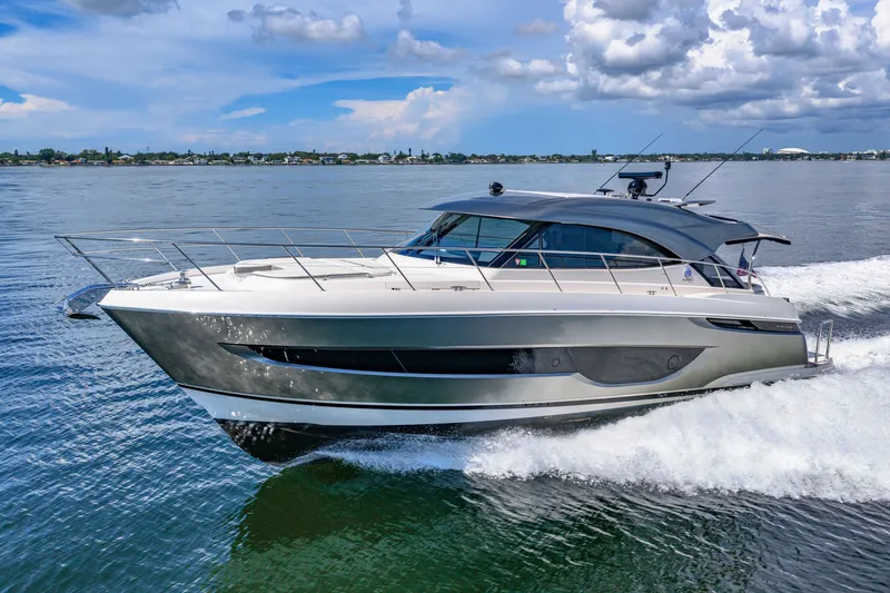 Slide: The Image of 2024 Riviera 4600 Sport Yacht Platinum Edition cruising on open water under a cloudy sky. - 14