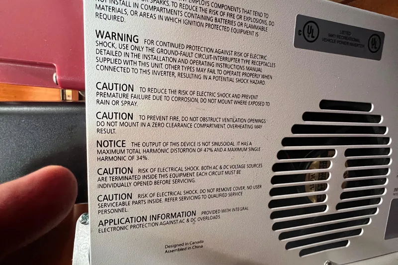 Slide: The Image of Warning and caution labels on a Beneteau Oceanis 473 inverter, emphasizing electrical safety. - 100