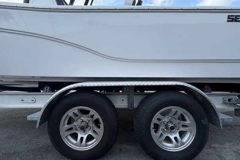 Slide: The Image of 2025 Sea Fox 251 Bay Fox boat on trailer, showcasing dual wheels and sleek design. - 87