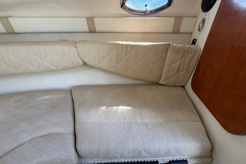 Slide: The Image of Interior cabin of a 2007 Sea Ray 240 Sundancer with beige cushions and a small window. - 62