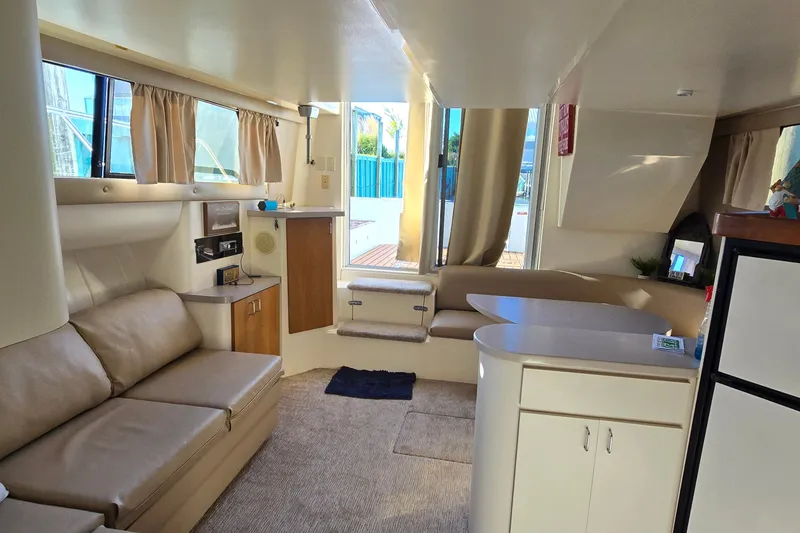 Slide: The Image of 1994 Mainship 40 Sedan Bridge interior with beige seating, kitchenette, and natural light. - 33