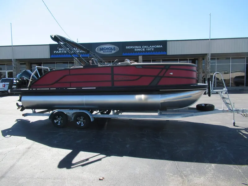 The Image of A red pontoon boat, Evotti 521CS model from 2027, sits on a trailer in front of a store. - 0