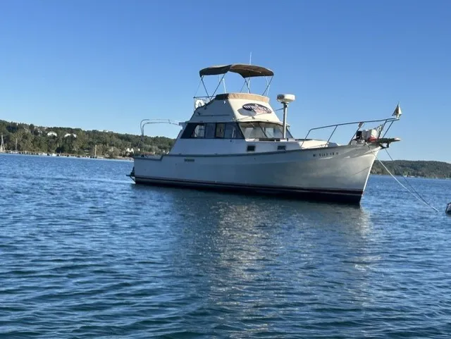 Slide: The Image of A 1979 Mainship 34 Trawler anchored on calm water, surrounded by green hills. - 2