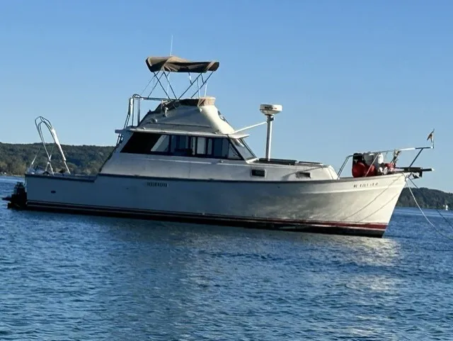 The Image of A 1979 Mainship 34 Trawler on calm water, featuring a covered helm and clear view of the shoreline. - 0