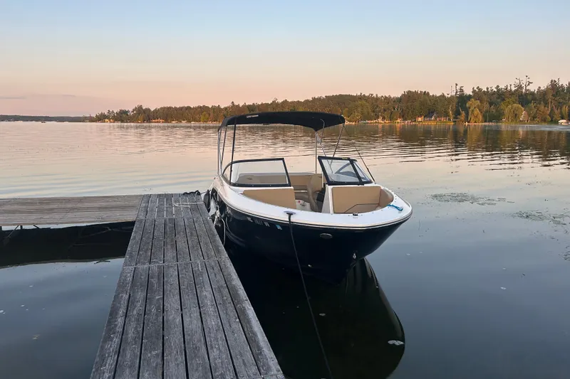 The Image of 2025 Bayliner V20i boat docked on a serene lake at sunset. - 0