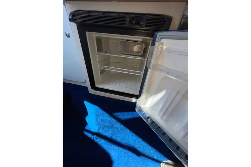 Slide: The Image of Open mini fridge inside a 2002 Fountain 35 Lightning boat, with blue carpet flooring. - 30