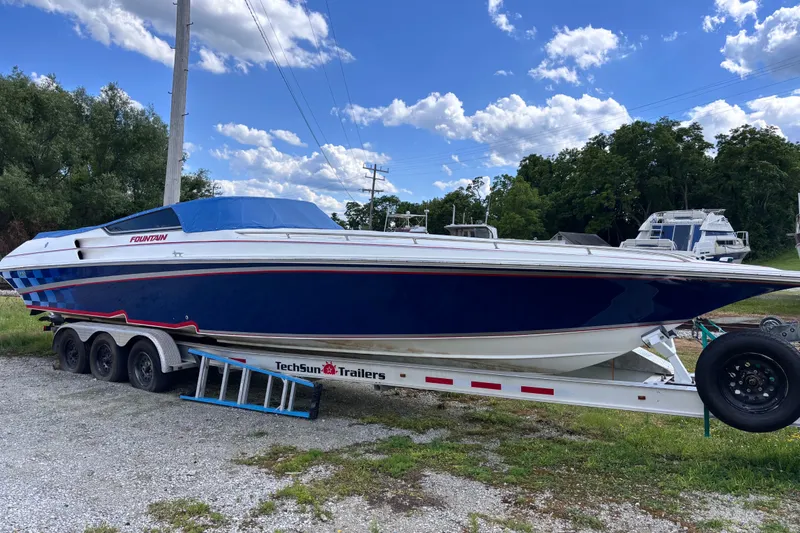 The Image of 2002 Fountain 35 Lightning boat on TechSun trailer, parked outdoors under blue sky. - 0