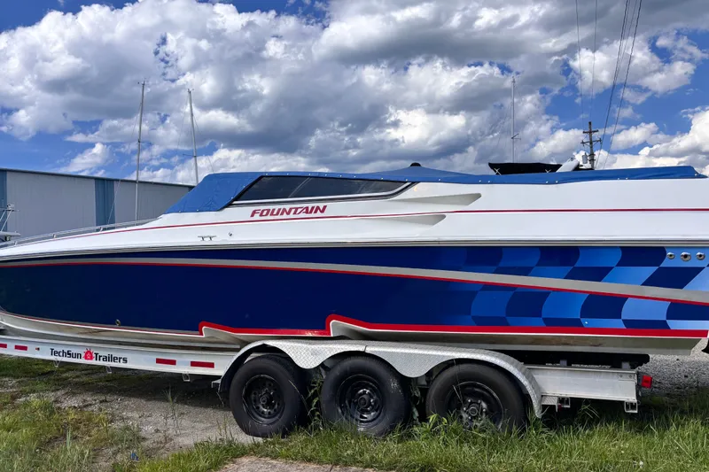 Slide: The Image of 2002 Fountain 35 Lightning speedboat on trailer, featuring blue and white design under cloudy sky. - 1