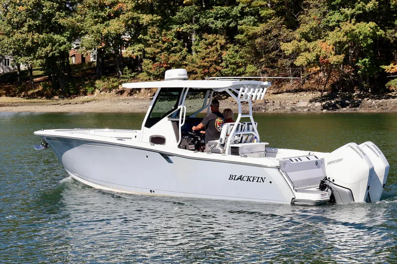 Slide: The Image of 2023 Blackfin 272 CC boat cruising on a serene lake with lush forest backdrop. - 1