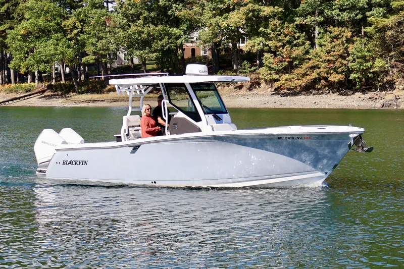 Slide: The Image of 2023 Blackfin 272 CC boat cruising on a scenic lake with lush green trees. - 2