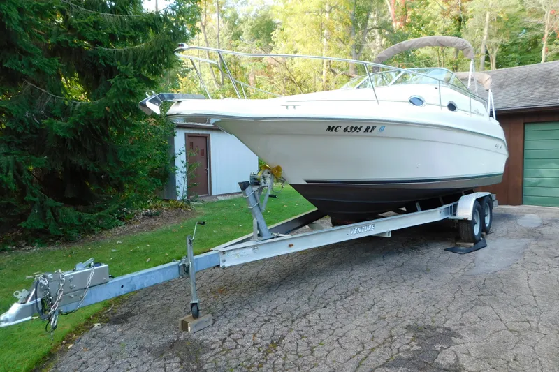 Slide: The Image of 1996 Sea Ray 250 Sundancer boat on trailer, parked outdoors near trees and a garage. - 4