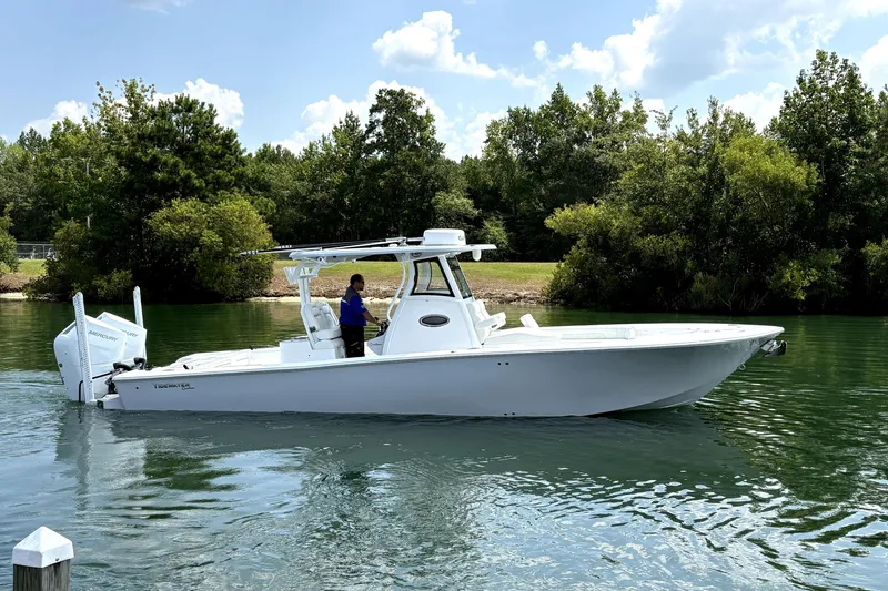 Slide: The Image of 2027 Tidewater 3100 Carolina Bay boat cruising on a serene waterway with lush greenery. - 2