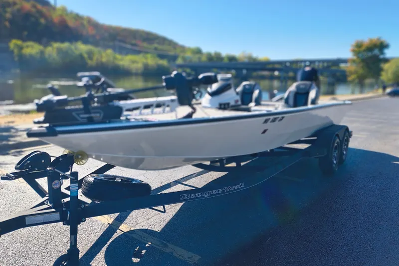 Slide: The Image of 2025 Ranger ALPHA 208 boat on trailer by scenic riverside, under clear blue sky. - 31
