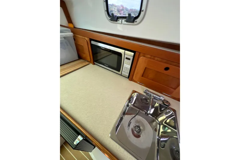 Slide: The Image of 2012 Hunt Yachts Surfhunter 29 interior kitchen with sink, microwave, and wooden cabinetry. - 16