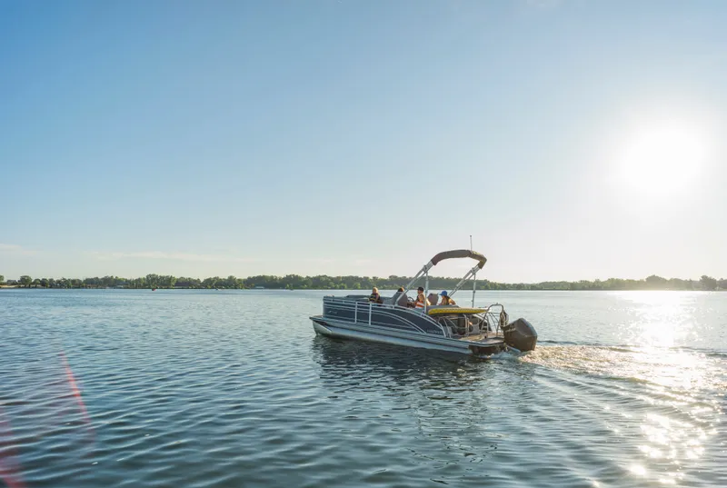 Slide: The Image of A 2023 Harris Solstice 230 pontoon boat cruising on a calm lake under sunny skies. - 13