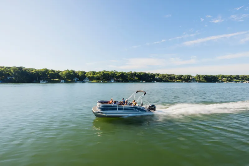 Slide: The Image of A Harris Solstice 230 pontoon boat speeds across a calm lake under a clear sky. - 18