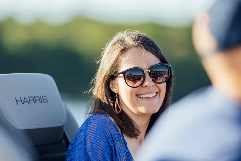Slide: The Image of A woman wearing sunglasses sits on a Harris boat, smiling. - 31