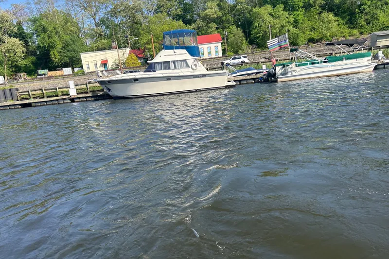 Slide: The Image of 1988 Silverton 37 Convertible yacht docked by a scenic riverside with lush greenery. - 5
