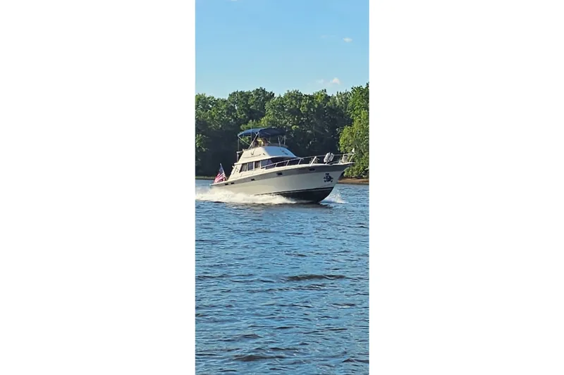 Slide: The Image of 1988 Silverton 37 Convertible yacht cruising on a scenic river with lush greenery. - 7