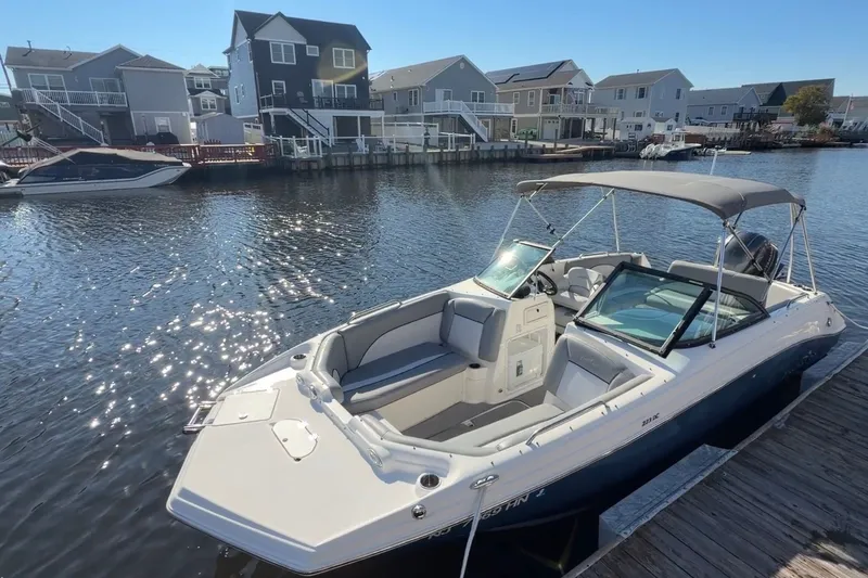 The Image of 2021 NauticStar 223 DC boat docked by waterfront homes under clear blue sky. - 6