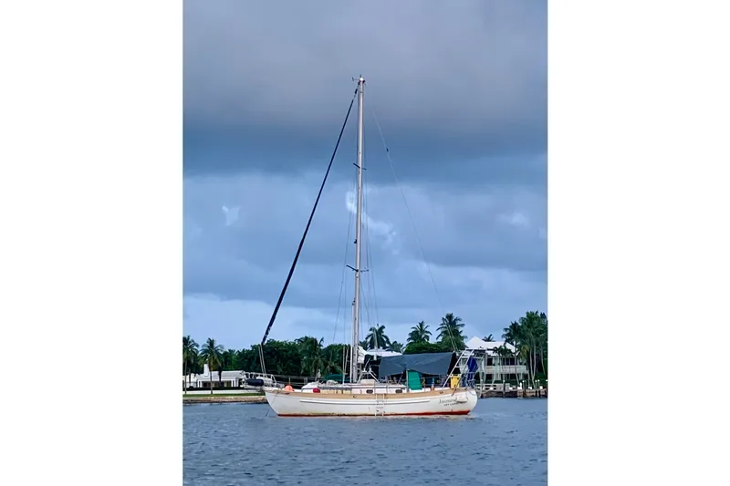 Slide: The Image of 1979 Tayana 37 sailboat anchored on a calm waterway under cloudy skies. - 2
