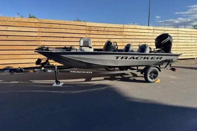 The Image of 2027 Tracker Pro Team 175 boat on trailer, parked outdoors against wooden fence. - 0