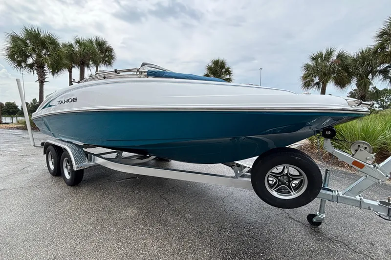 Slide: The Image of 2027 Tahoe 2150 CC boat on trailer, parked near palm trees under cloudy sky. - 2
