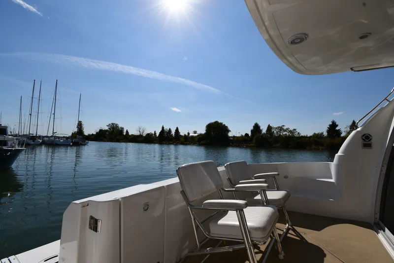 Slide: The Image of 2003 Cruisers Yachts 5000 Sedan Sport deck with chairs, overlooking serene water and sailboats. - 17