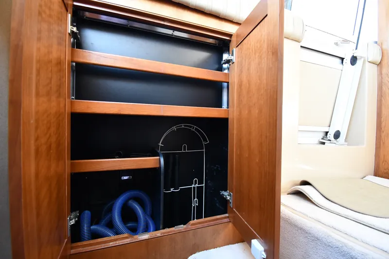 Slide: The Image of Open wooden cabinet inside 2003 Cruisers Yachts 5000 Sedan Sport, revealing storage space and blue hose. - 57