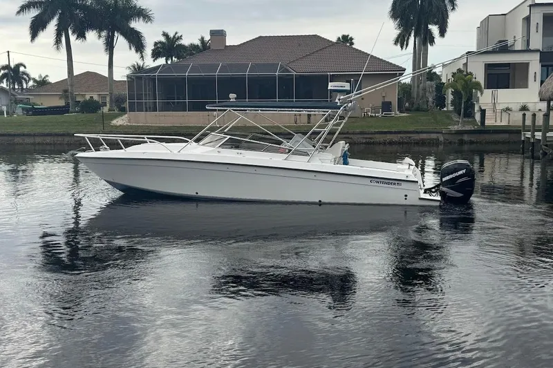 Slide: The Image of 2001 Contender 35 Side Console boat on calm water, with palm trees and houses in the background. - 5