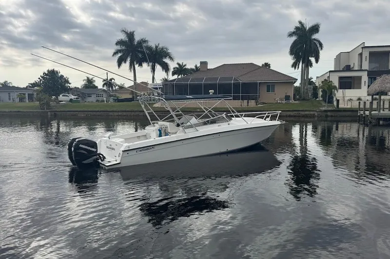 Slide: The Image of 2001 Contender 35 Side Console boat on calm water, with palm trees and houses in the background. - 2