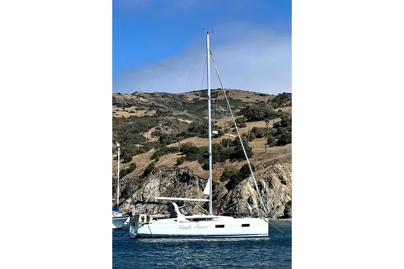 The Image of 2014 Beneteau Oceanis 38 sailboat anchored near rocky coastline under clear blue sky. - 0