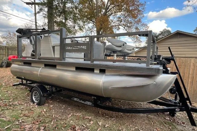 The Image of 2026 Lake Lounger 16' Front Fish Pro pontoon boat on trailer, parked outdoors. - 0