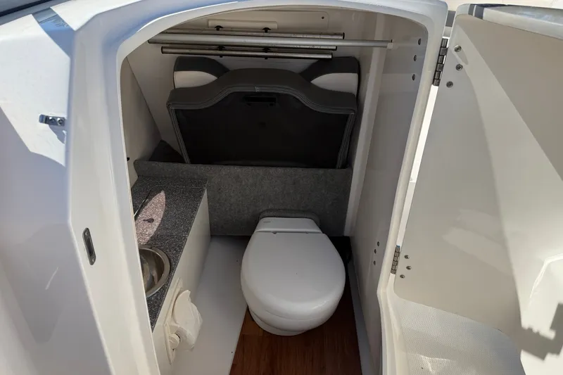 Slide: The Image of Interior of 2016 Chaparral 250 Suncoast boat featuring a compact bathroom with toilet and sink. - 18