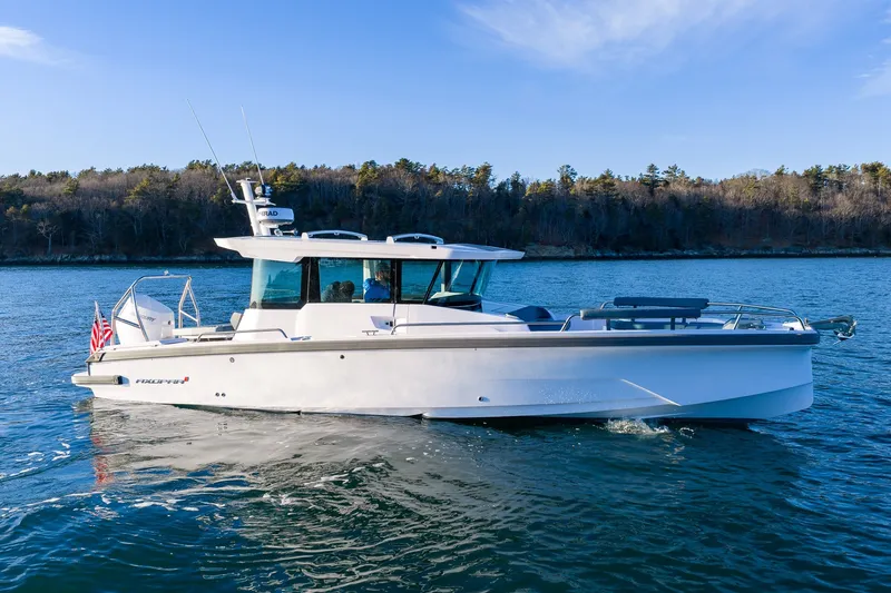The Image of 2026 Axopar 29 XC Cross Cabin boat cruising on a serene lake with forested shoreline. - 0