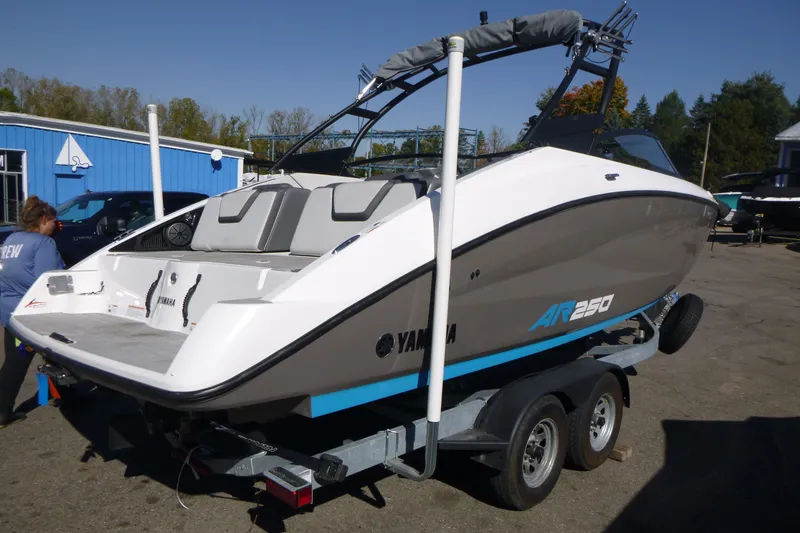 Slide: The Image of 2022 Yamaha Boats AR250 on trailer, parked outdoors near blue building. - 2