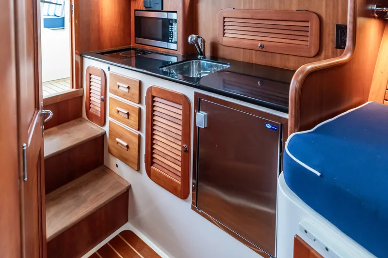 Slide: The Image of 2013 Hinckley Talaria 34 yacht interior with wooden cabinetry, kitchenette, and stairs. - 26