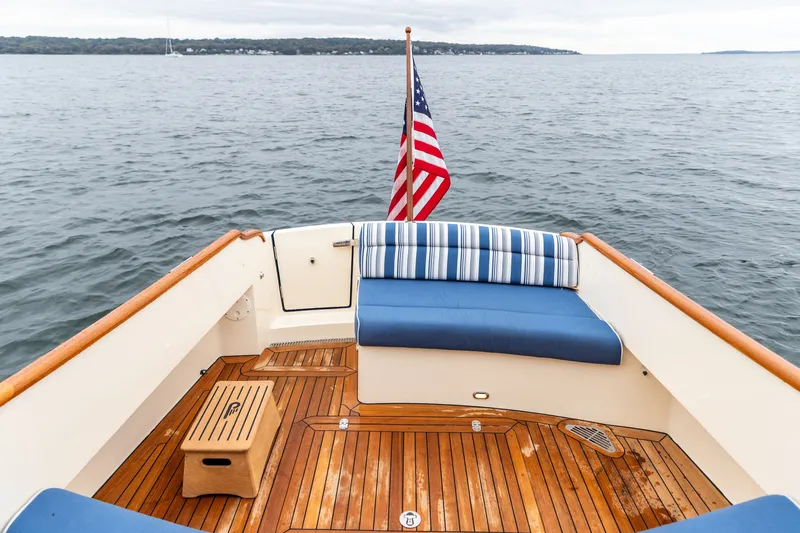 Slide: The Image of 2013 Hinckley Talaria 34 boat deck with striped seating and American flag on calm water. - 13